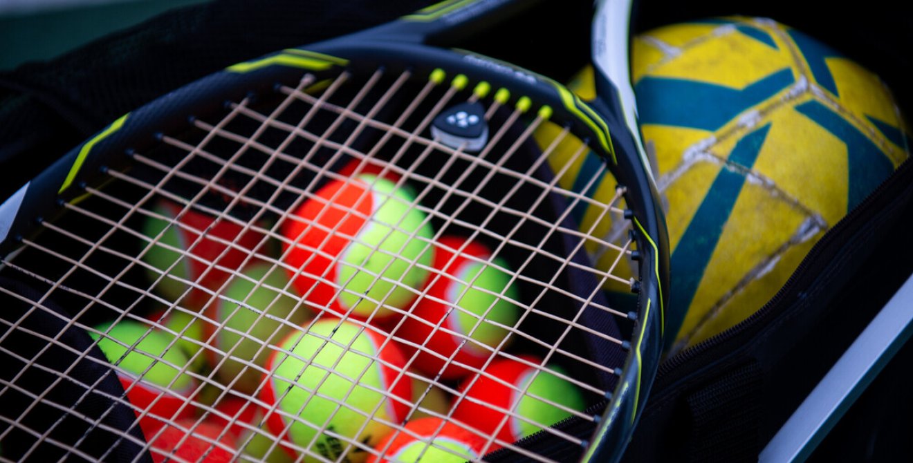 A tennis racket, tennis balls and a football in a kit bag