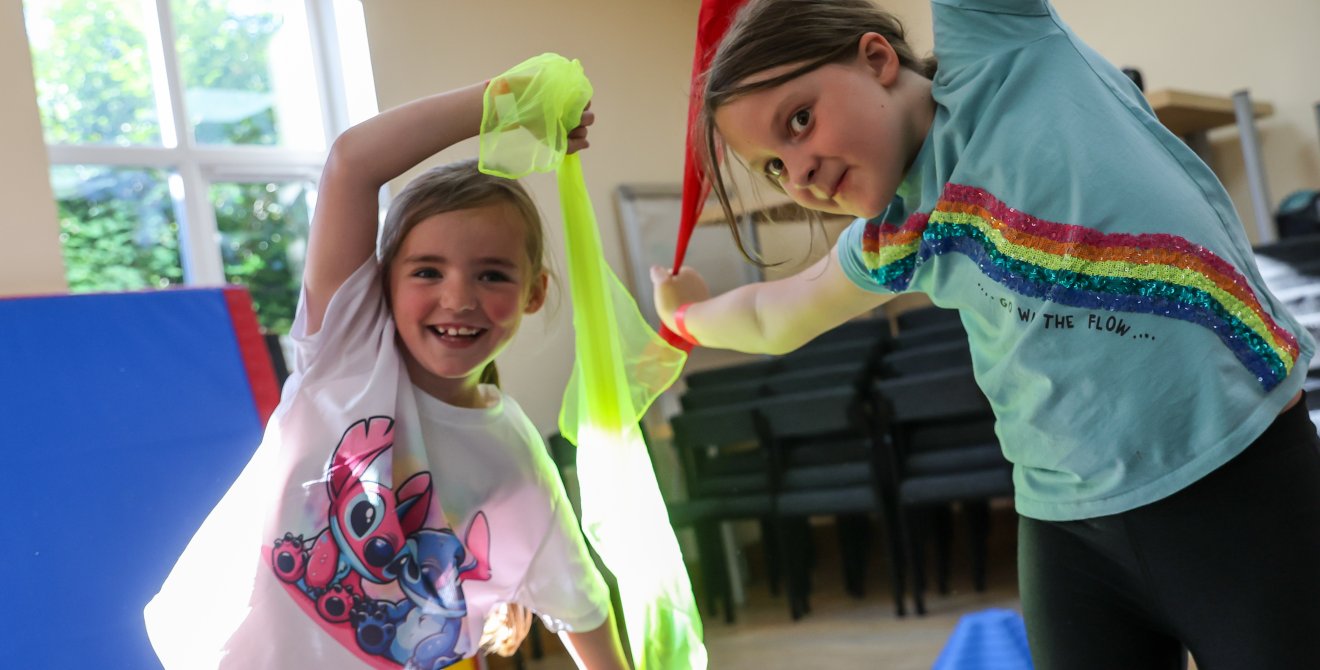 Plant yn chwifio rhuban lliwgar mewn dosbarth gymnasteg.