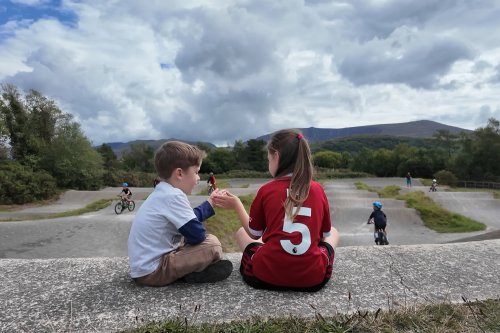 Two children sat in front of a bike track.