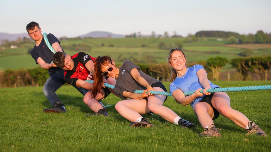 A group of young people tugging a rope and leaning back.