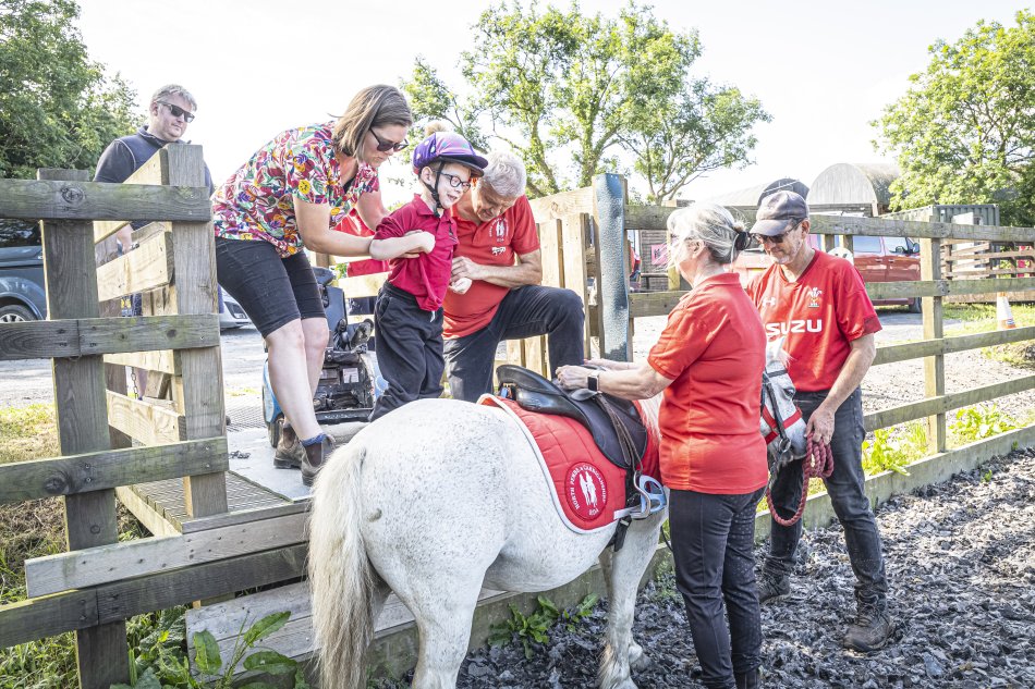 Two volunteers help Iori onto the horse