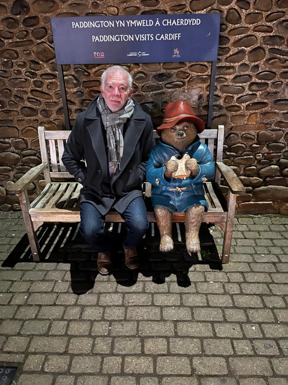 Brian Davies sitting next to a statue of Paddington on a bench